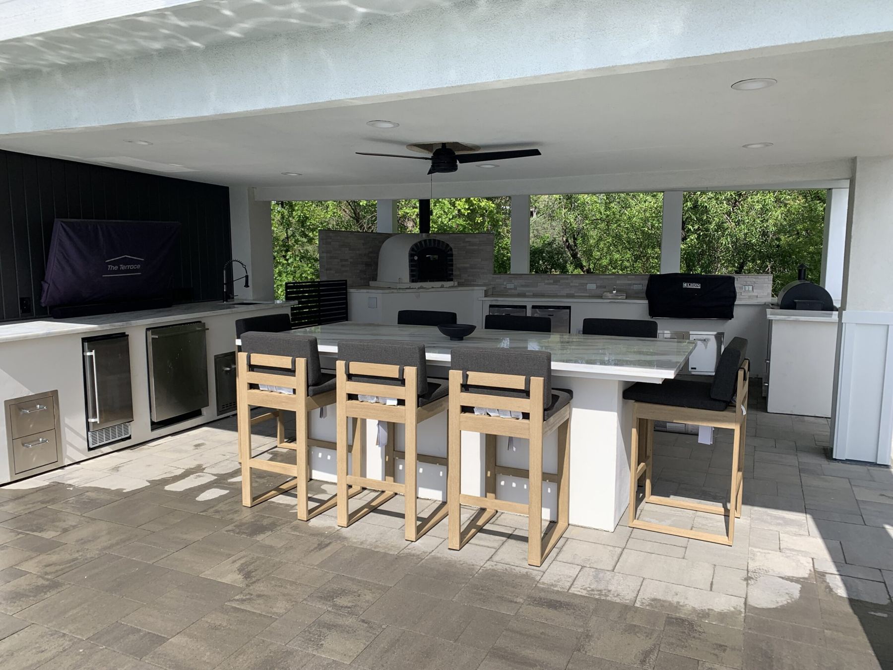Covered patio kitchen with seating bar, wood bar stools and pizza oven