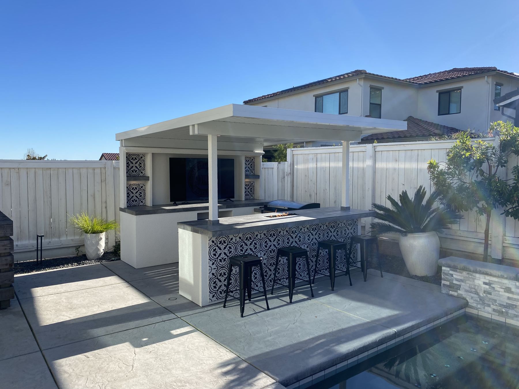 Daytime TV island with white roof, patterned tile bar and stools beside a pool